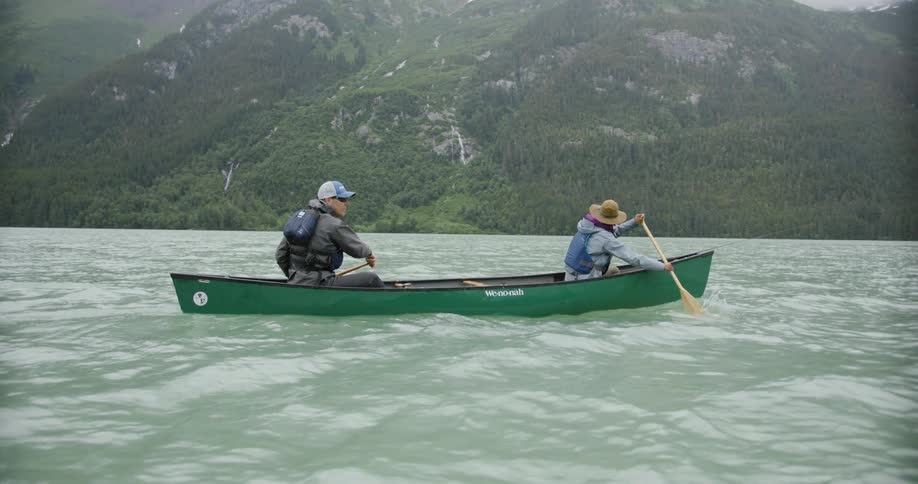 Two people paddling a green canoe on a lake surrounded by mountains