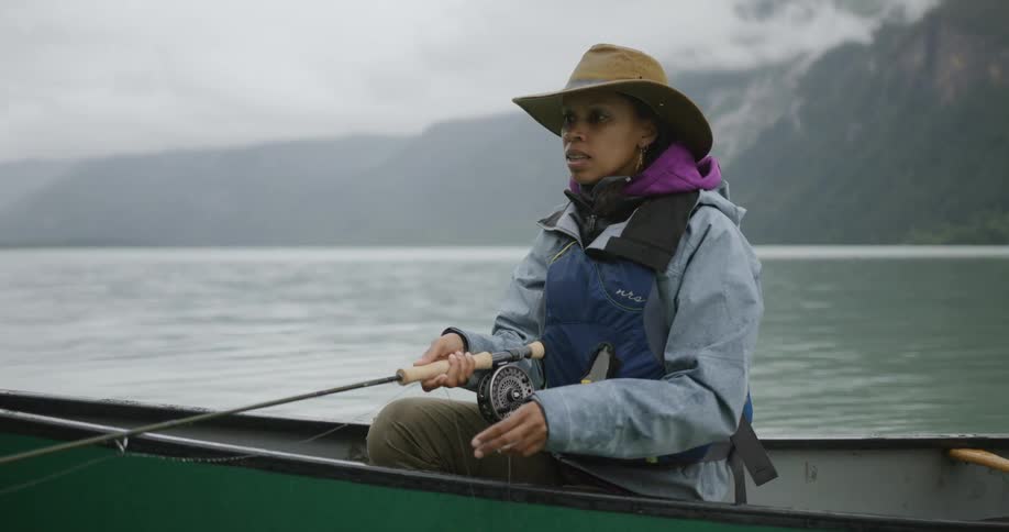 A woman sitting in a canoe holds her fishing rod while pulling the fishing line