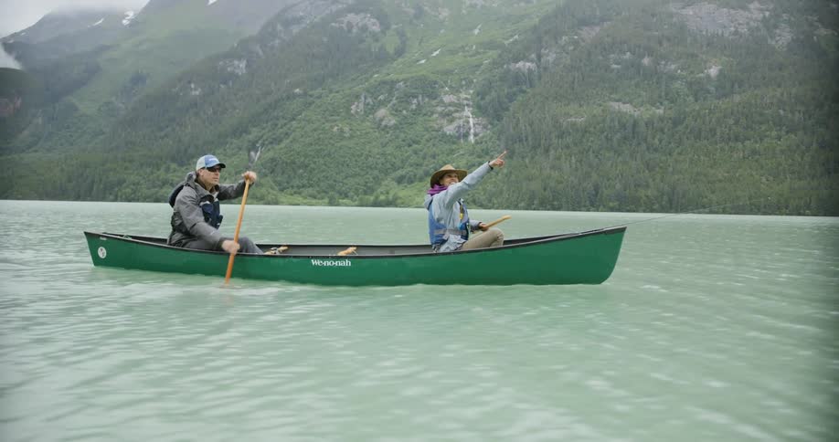 Man and a woman paddling a canoe across the sea with mountains in the background