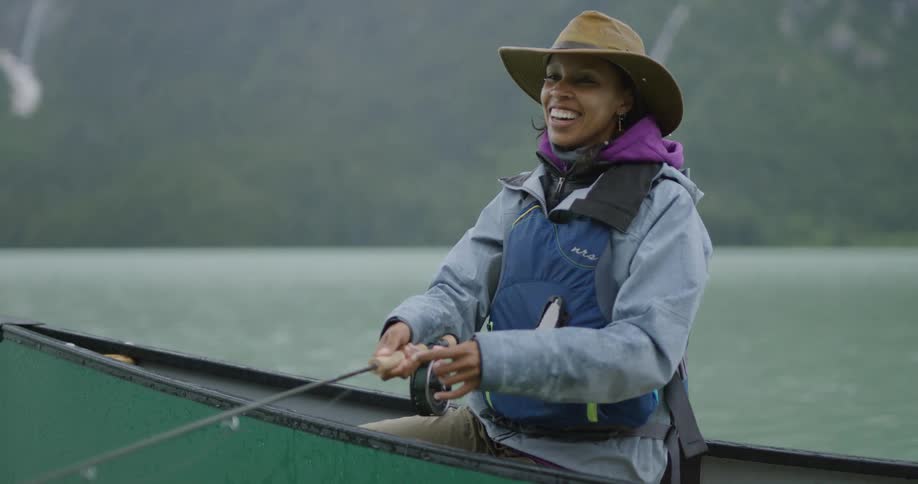 Smiling woman wearing a hat and life vest fishing from a canoe on a lake