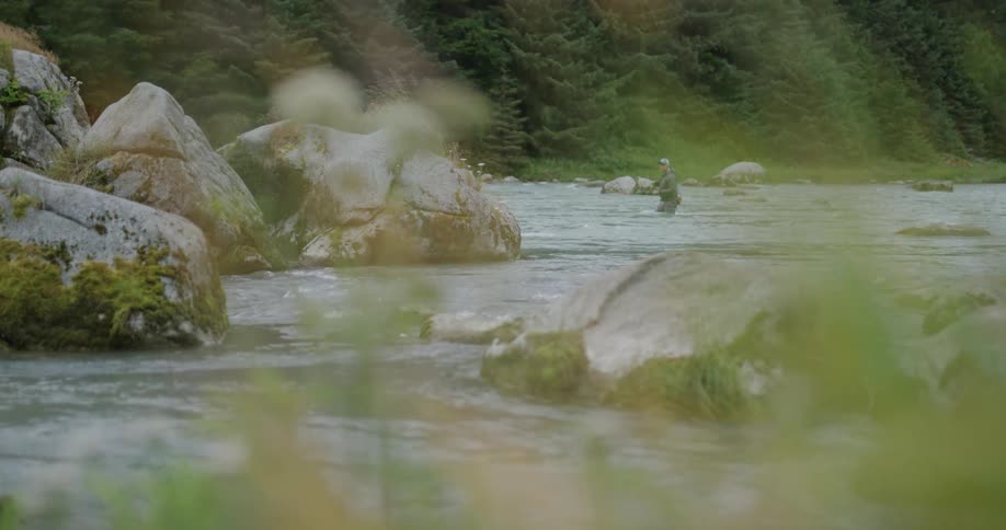 Fisherman in the background of a river partially hidden by rocks and vegetation