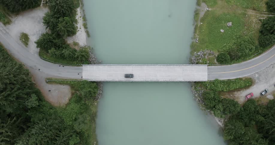Car crossing a narrow bridge over a clearwater river captured from an aerial view