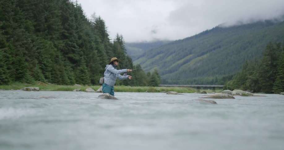 The woman is knee high in the river and fly fishing
