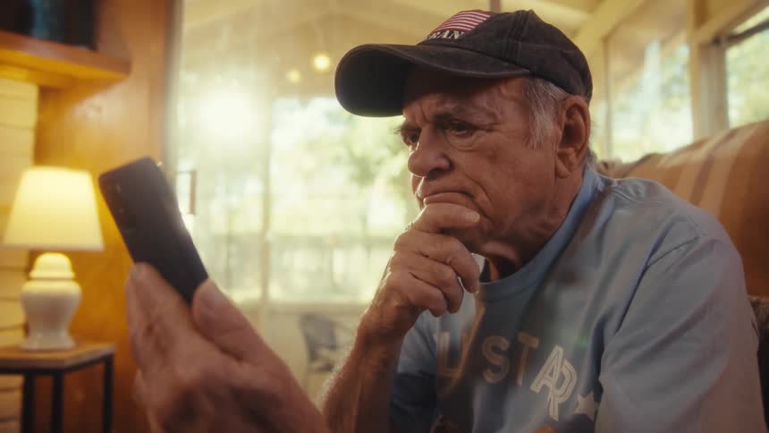 Man wearing a cap and blue shirt looks attentively at a cellphone