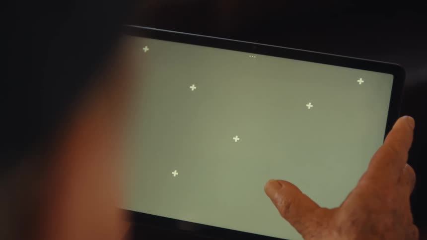 An elderly man is holding a digital tablet with a hand positioned on the screen and swiping on the screen