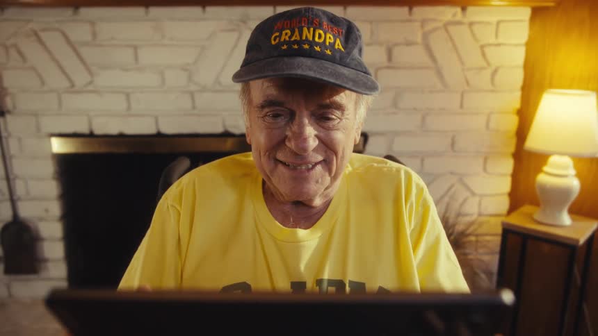 Elderly man wearing a yellow tshirt with the words us army veteran and a hat labeled grandpa holding a tablet in his hands