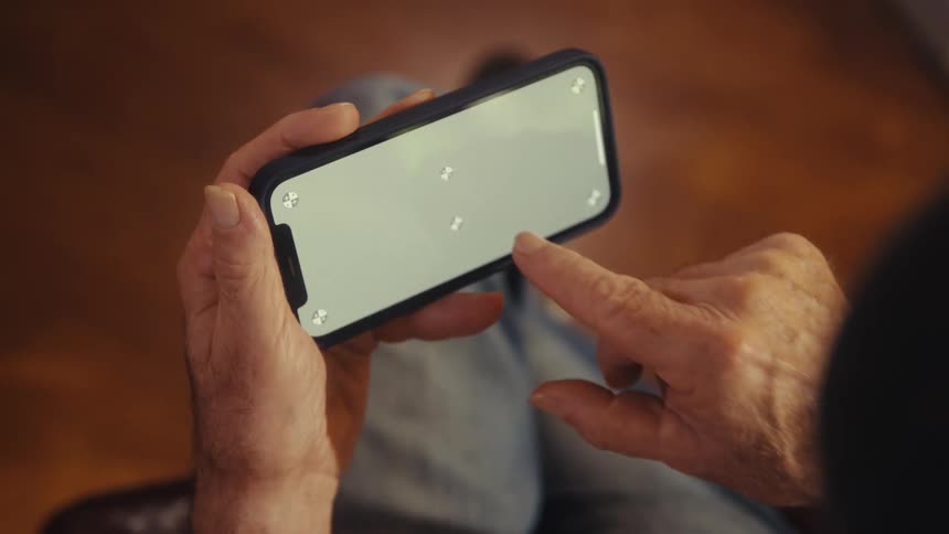 Elderly man scrolls on a smartphone while sitting indoors