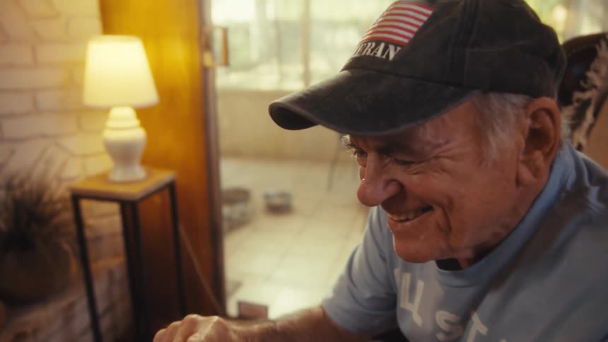 Smiling elderly man wearing a black cap and light blue tshirt while looking at a cellphone