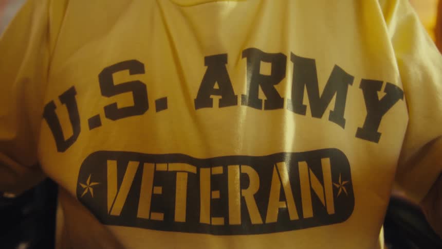 Chest of a white man sitting down wearing a t shirt saying us army veteran indoors during day time
