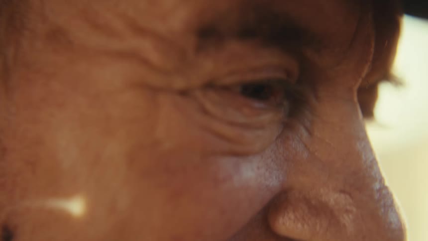 A closeup side profile shot of an older mans face reveals his joyous wrinkled smile he closes his eyes and tilts his head back laughing at something offscreen