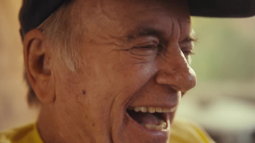 In the video a closeup shot shows a mans face as he smiles widely and laughs his mouth is open revealing his teeth and gums as he reacts to something offcamera with visible amusement
