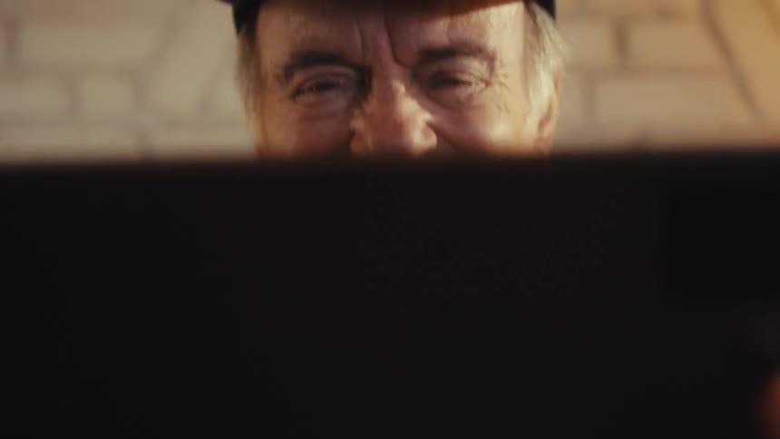 Elderly man sitting in his living room at midday watching a game on his ipad and bursting with excitement