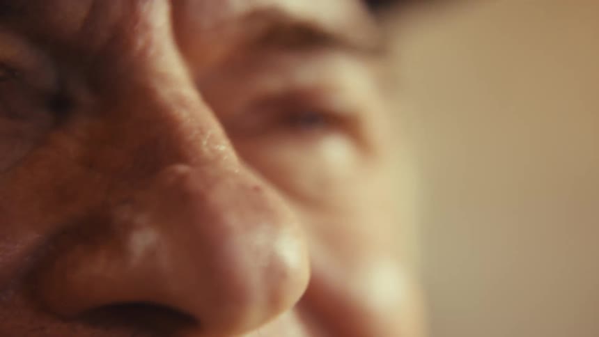 Elderly man wearing a hat sitting indoors in his living room suddenly filled with excitement