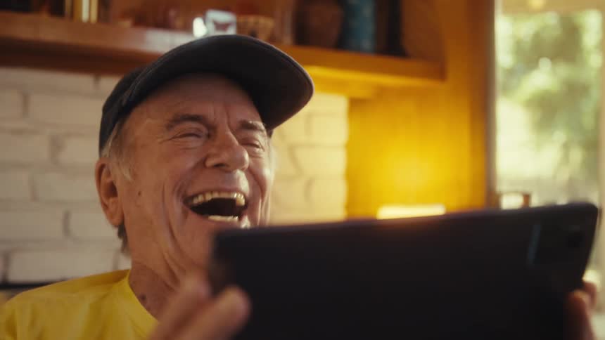 Elderly man sitting in his living room at midday watching a game on his ipad and bursting with excitement