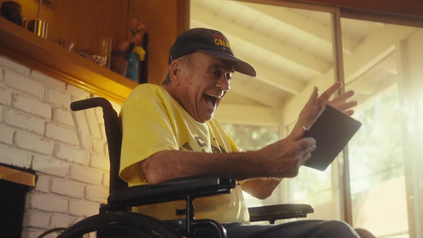 Man in a wheelchair holds a tablet in a sunlit room