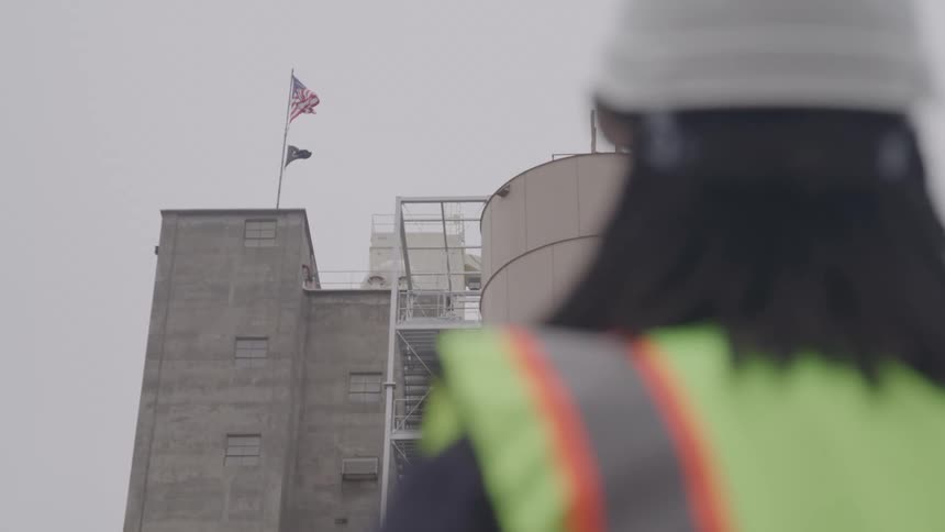 A worker in a safety vest looks at an industrial building on site