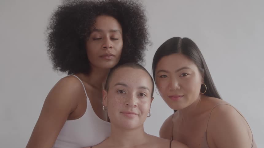 A medium closeup shot shows three women with diverse skin tones hair types and features posing together they are looking directly at the camera with a confident neutral expression