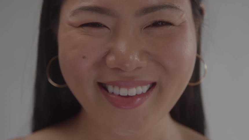 A closeup shot focuses on a womans face as she looks directly at the camera her expression changes from a serious look to a joyful smile