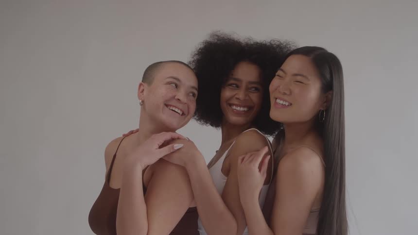 A group of three women laugh and smile as they pose together for a photo the woman on the right has her arm around the woman in the center and they are all wearing similar tank tops