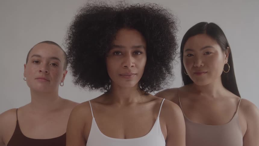 A powerful studio portrait features three ethnically diverse womenone black with an afro one asian and one with a shaved headstanding together and looking directly at the camera with calm serious expressions