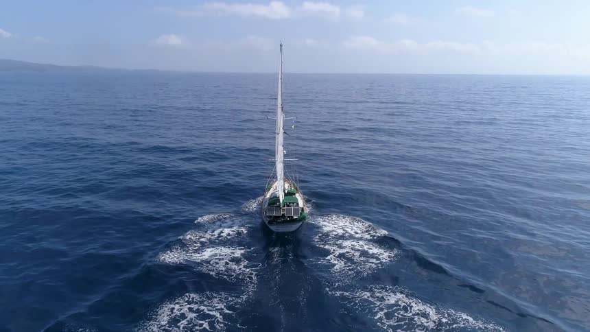 A sailboat moves across the ocean surface towards a coastal area