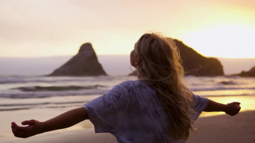 A woman stands on the beach and holds her arms out sideways