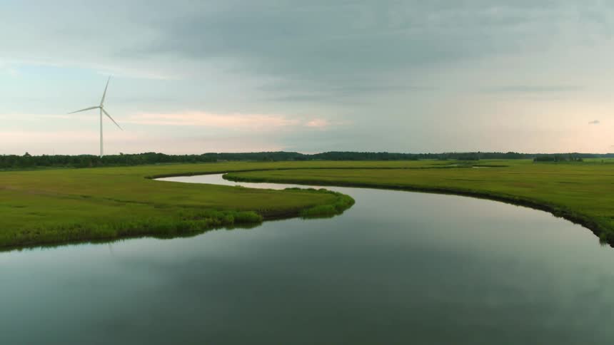 Aerial flyover of a curved waterway and a wind turbine nearby