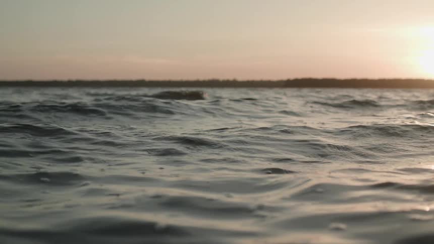 The surface of the water moves and reflects the light from the sky with land visible in the background