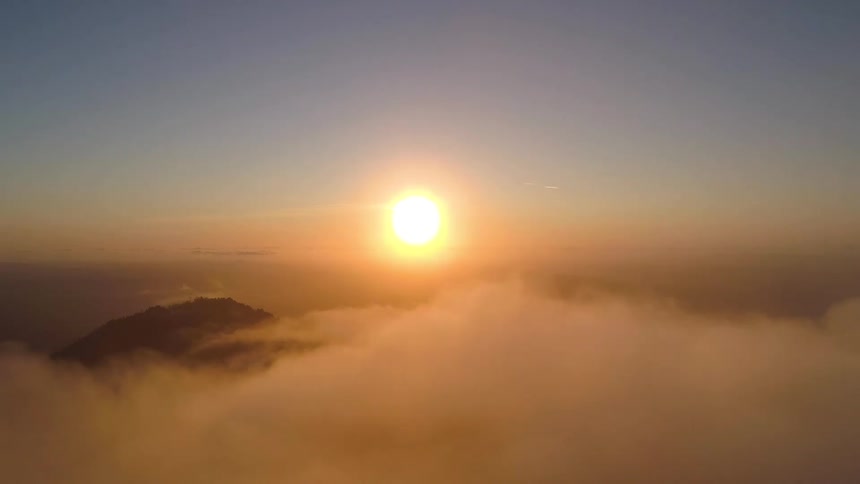 The sun rises and illuminates a field of clouds with a mountain peak emerging in the center