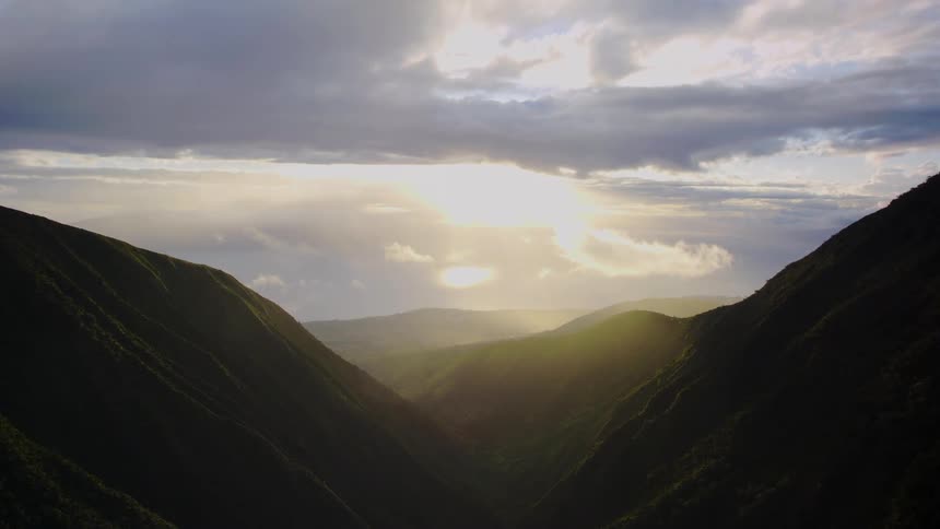 Sun shines through a break in the clouds onto a foggy valley in the mountains