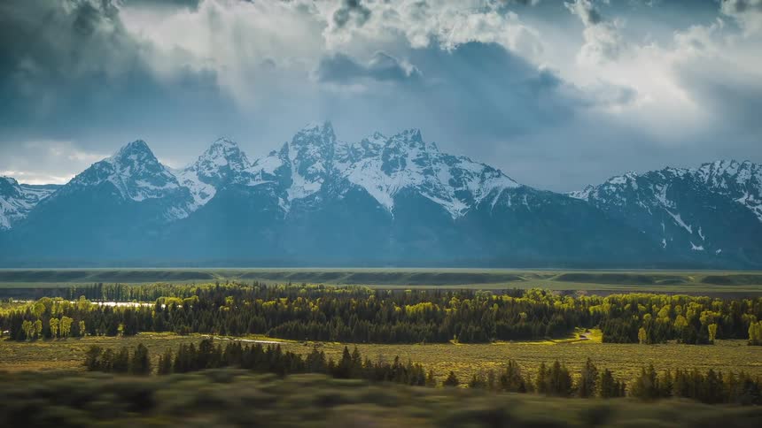 A towering mountain range is covered with snow under a cloudy sky