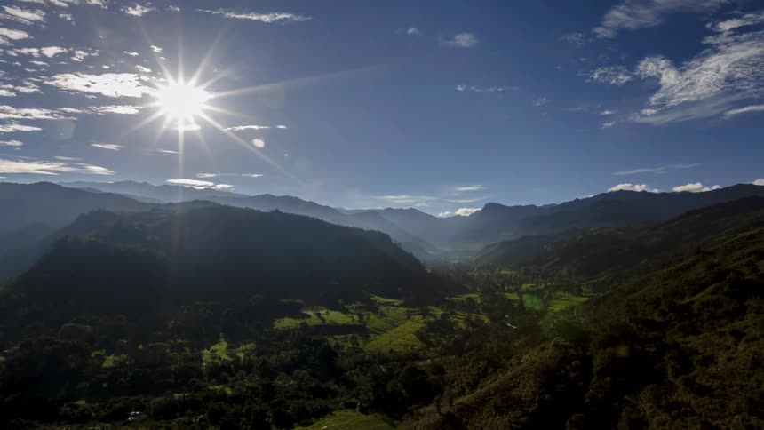 Sun rises into the sky above a mountain range on a cloudy day