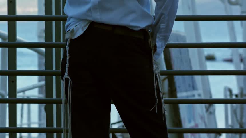 Lower half of person standing outside behind a metal fence