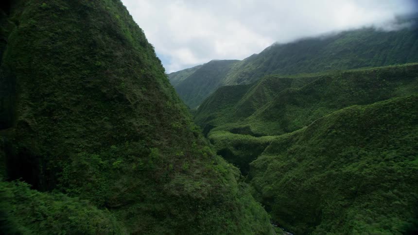 Dense vegetation covers the mountainous terrain surrounding a narrow river valley on a cloudy day