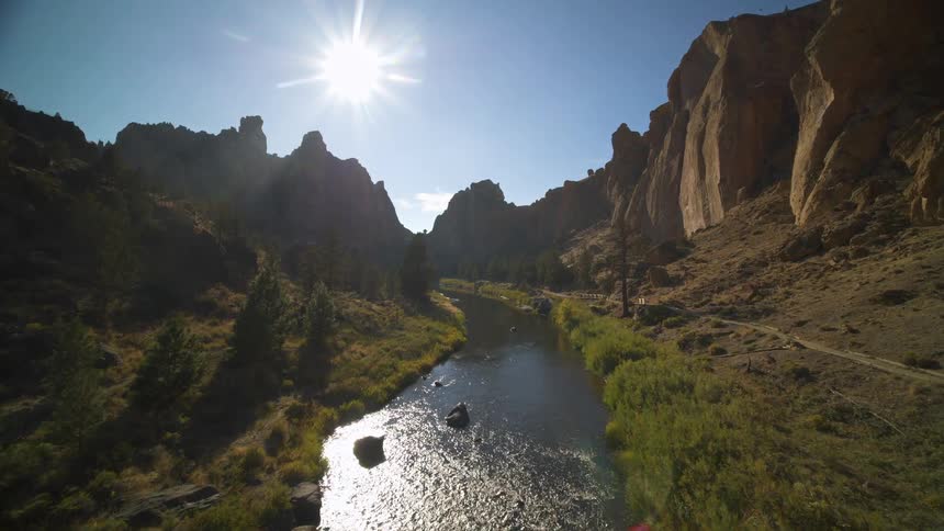 A serene river flows through a rocky canyon on a bright sunny day the camera slowly moves over the water which reflects the blinding sun as it travels between the tall canyon walls