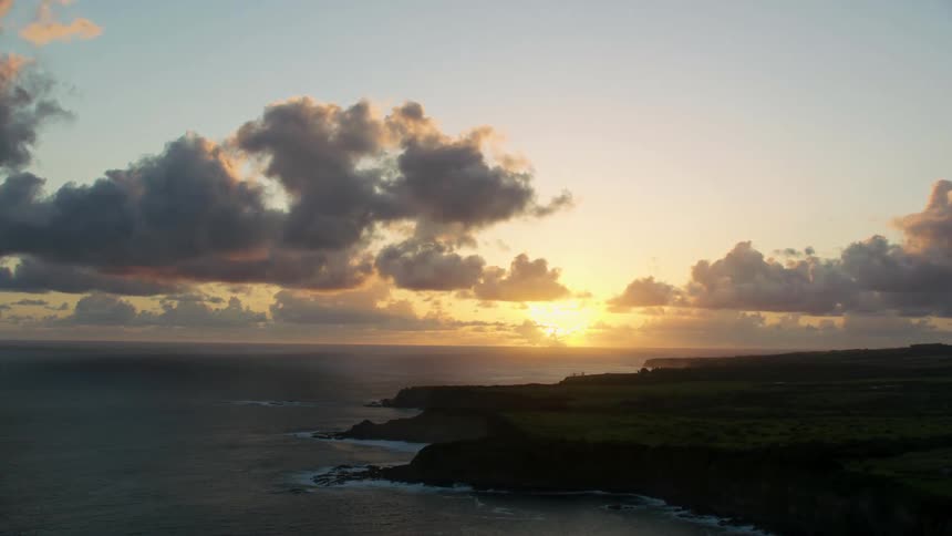 A shot shows an ocean land and sky with a sun setting on the horizon