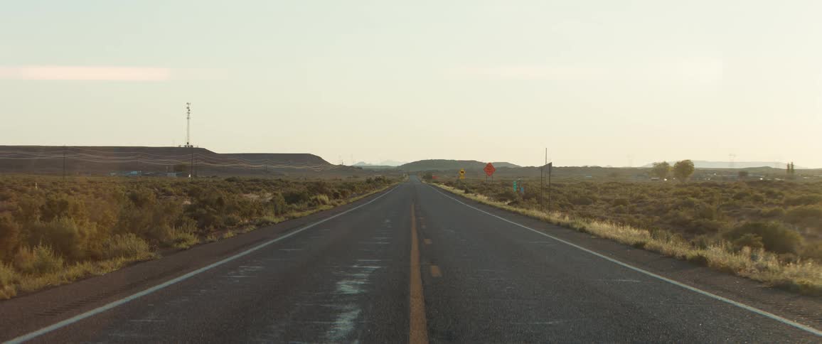 A long empty desert highway stretching towards distant hills under a hazy sky at dawn or dusk