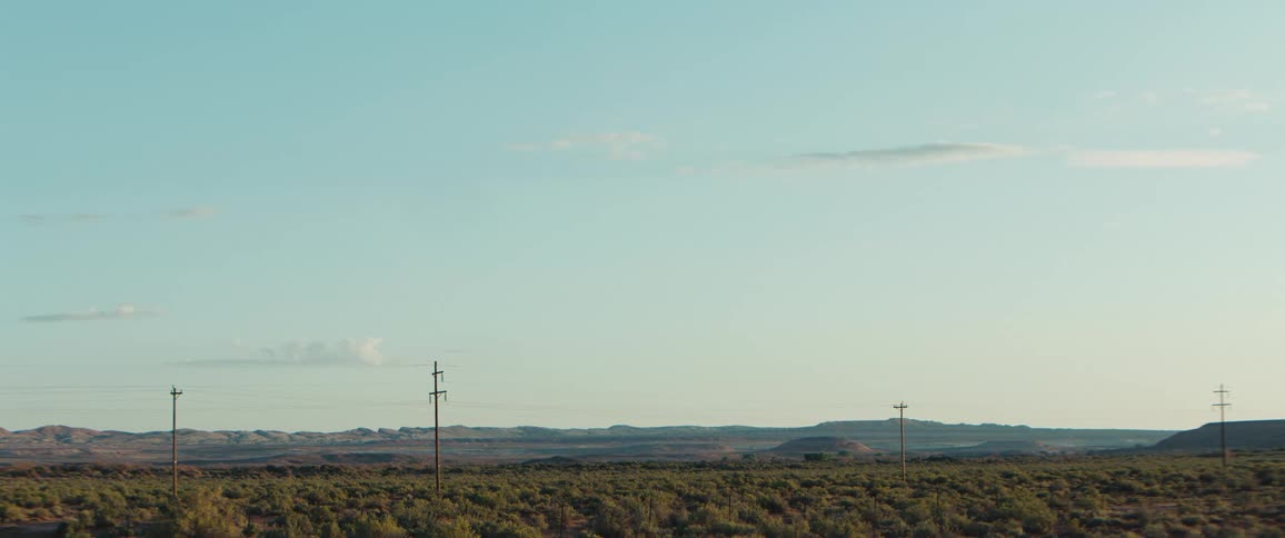 Power poles cross a green plain under a clear sky