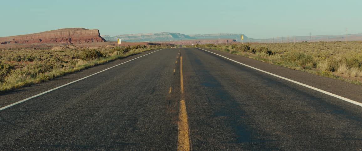 An empty road stretches with distant mountains into the desert