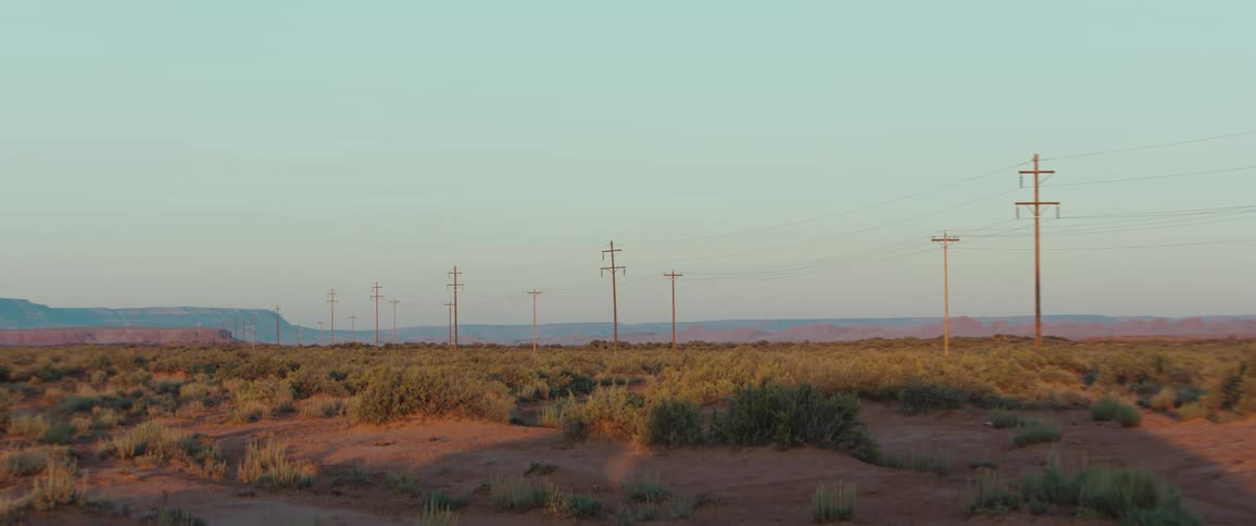 Desert scrubland with shrubs stretching toward distant mesas at sunset