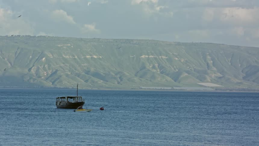 Smaller boat passes an anchored boat beside a mountain