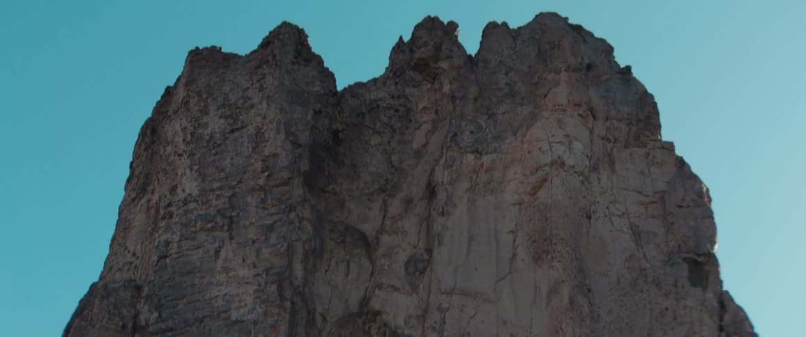 Brown craggy mountain contrasts against a light blue sky
