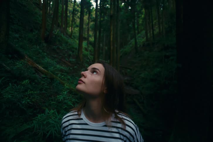 A woman gazes thoughtfully while standing in a dense forest