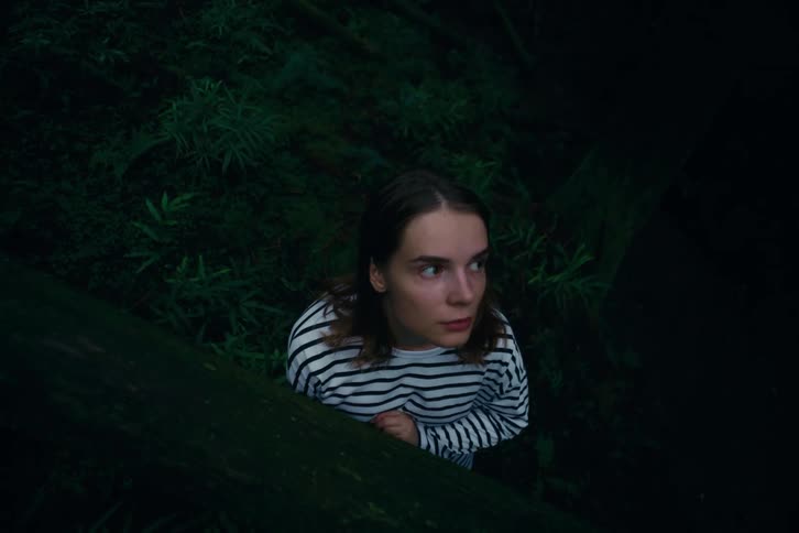Person in a white and black striped shirt looks upward amid dark vegetation