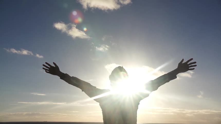 A man with outstretched arms is silhouetted by the sun
