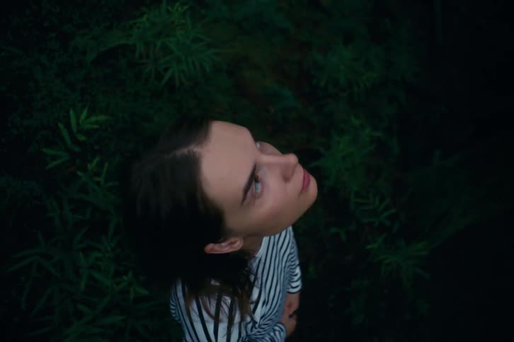 The girl is looking up while standing in the grass