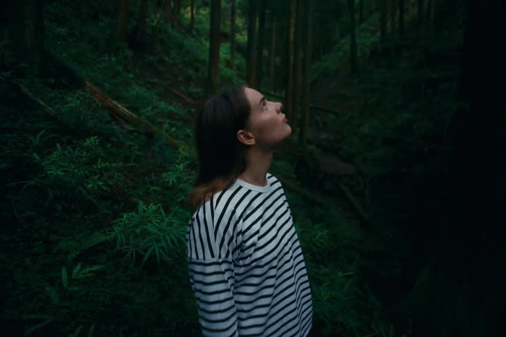 Woman in a striped shirt looks upward in the dense forest
