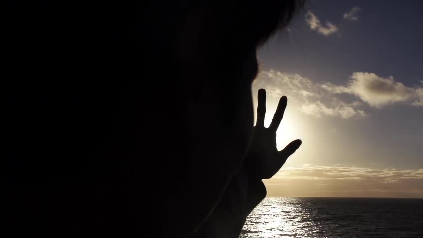 Person puts their hand up to the sun at sunset
