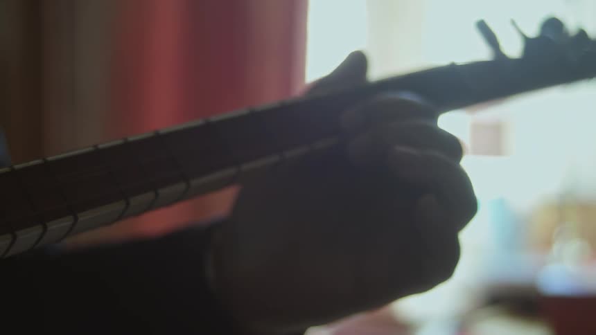 A man's hand strums the neck of a guitar
