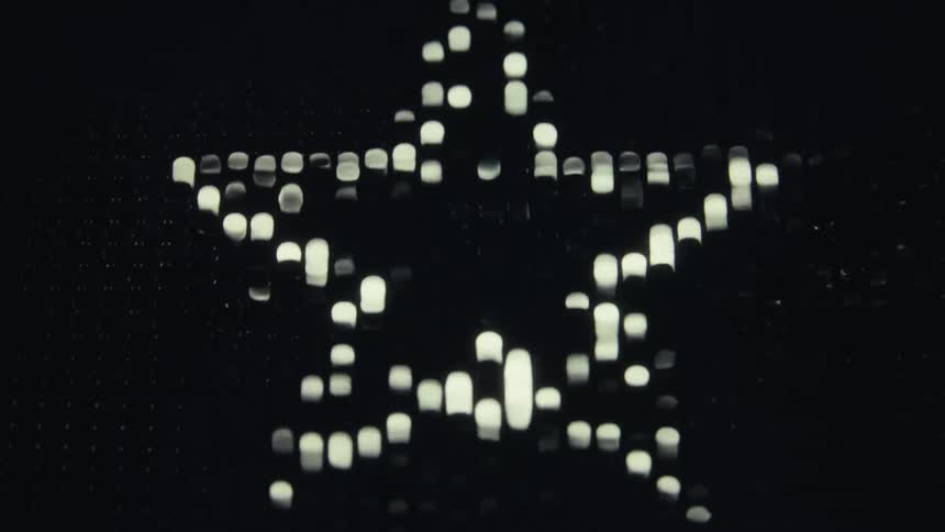 A pixelated white heart made of glowing ledlike dots changes into a star against a black background